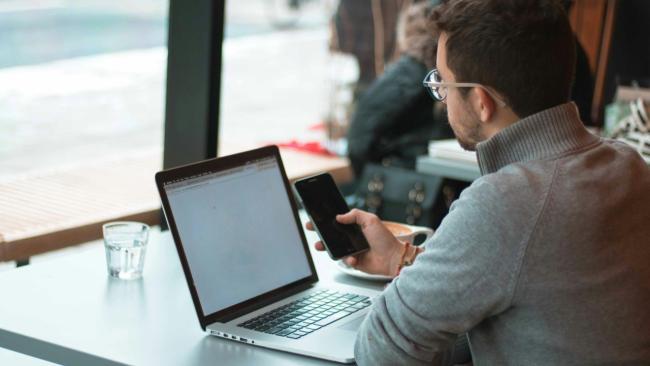 Uživatel kontroluje svůj mobil při práci na laptopu